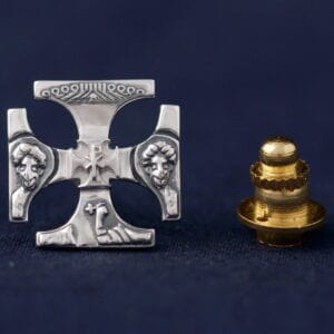 Sterling silver pin with intricate design on navy background, accompanied by a gold fastener.