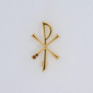 Gold Chi Rho pin with red gemstones on white background, religious symbol, Christian jewelry accessory.